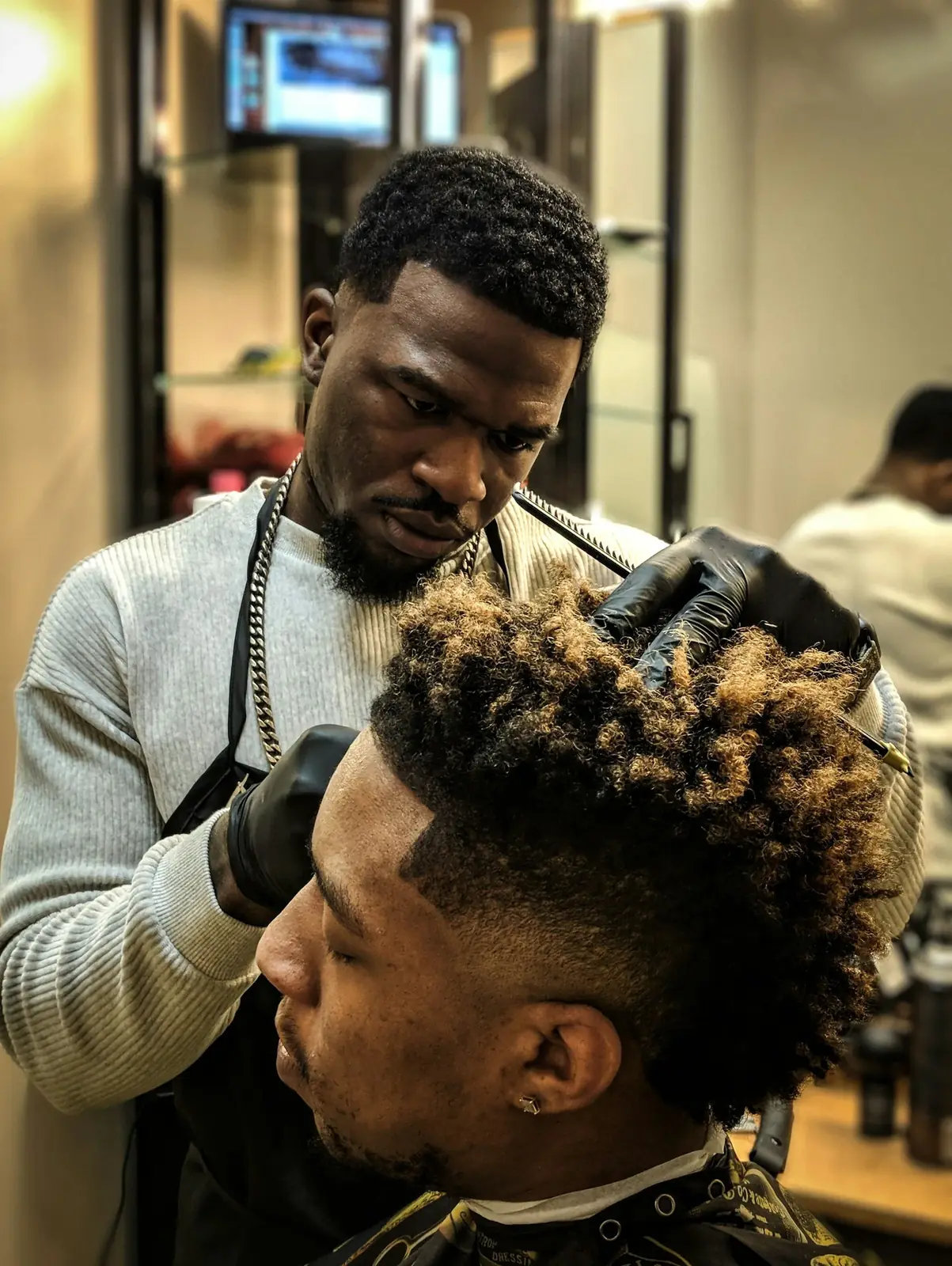 Barbering instructor fading a client's curly hair with clippers at Expert Barber & Beauty School in McKinney, TX