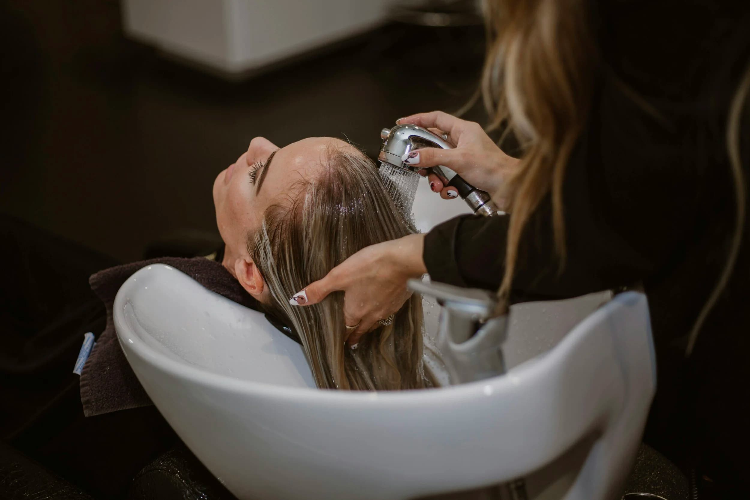 Stylist shampooing a client's hair at the backwash bowl, a fundamental taught in the Cosmetology Operator crossover program